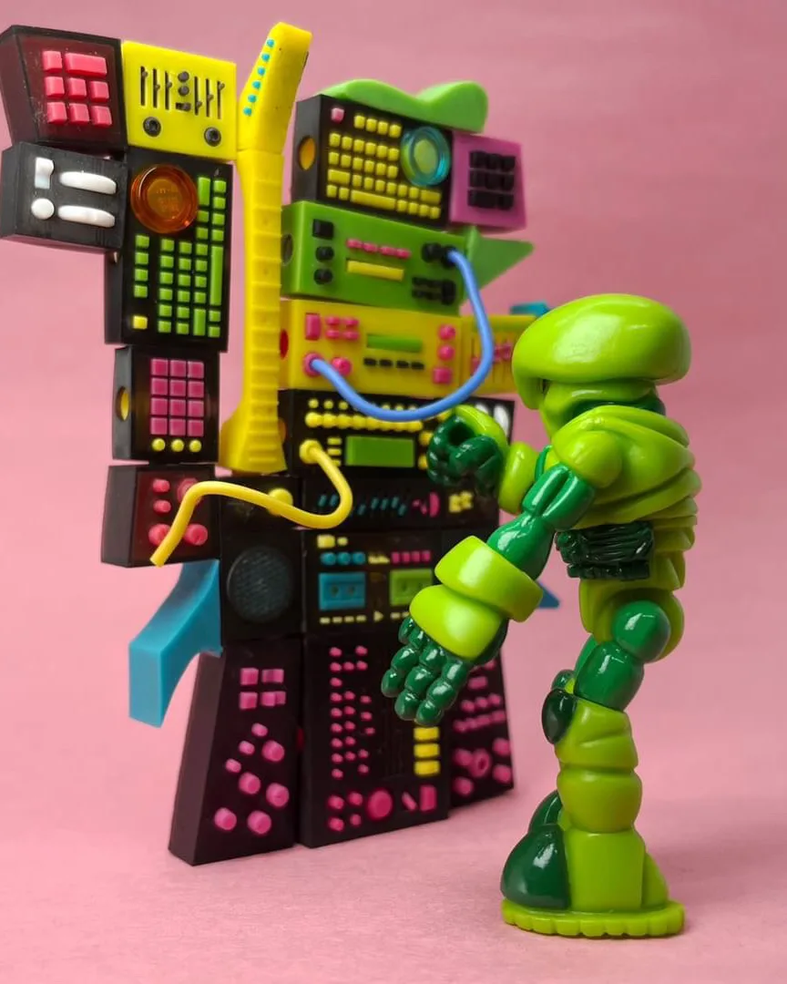 Green Glyos Pheyden figure beside a tall stack of brightly colored synth modules